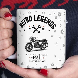 May include: White ceramic mug featuring a vintage motorcycle design with the text "Retro Legends" and "Vintage Garage Series - 1981 - DDR Two-Stroke." The mug has a black and white graphic of a motorcycle.