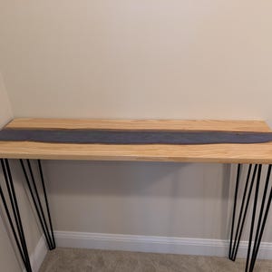 May include: A wooden console table with a light-colored wood top and a dark blue resin river design. The table has black hairpin legs. The table is approximately 48 inches long.
