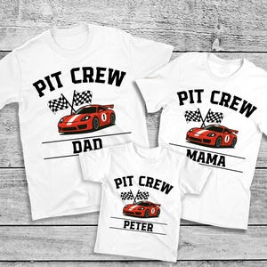 May include: White t-shirts with a racing theme. Each shirt features the words "PIT CREW" above a red race car and checkered flags. The shirts are labeled "DAD", "MAMA", and "PETER".