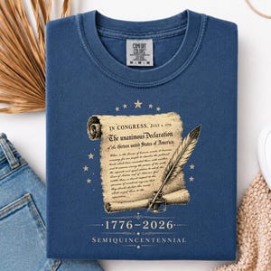 May include: Navy blue t-shirt featuring a graphic of the Declaration of Independence with a quill and inkwell. The text reads "IN CONGRESS, JULY 4, 1776" and "The unanimous Declaration of the thirteen united States of America." The shirt also has the text "1776-2026 SEMIQUINCENTENNIAL."