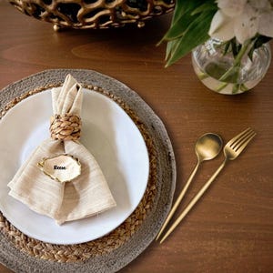 May include: A white ceramic mug with a black handle and the text "But First, Coffee" in a bold, black font. The mug is set against a blurred background, suggesting a cozy setting.