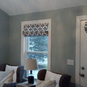 Peut inclure: Un salon avec deux fen&ecirc;tres et une porte, toutes avec des stores romains &agrave; motif g&eacute;om&eacute;trique gris et blanc. La pi&egrave;ce est peinte en bleu clair et comporte deux chaises avec des coussins blancs.