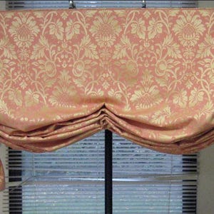 May include: Peach-colored window valance with a gold floral pattern. The fabric is gathered and draped, creating a decorative effect. The valance is designed to hang above a window, adding a touch of elegance to the room.