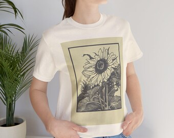 Könnte beinhalten: Cremefarbenes T-Shirt mit einer Schwarz-Weiß-Sonnenblumen-Illustration in einem rechteckigen Rahmen. Das Design zeigt eine detaillierte Zeichnung einer Sonnenblume mit Blättern und Stiel. Das Shirt ist ein Freizeitartikel.