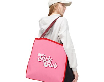 May include: Pink tote bag with red trim and straps. The bag features the text "Girls Club" in a retro white font. The bag is carried over the shoulder.