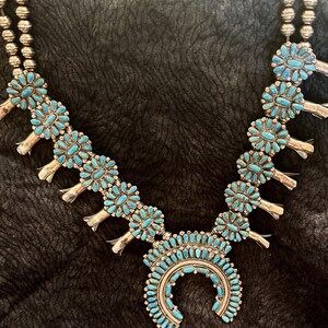 Puede incluir: Un collar de plata con piedras turquesas. El collar presenta un colgante en forma de media luna y diseños florales. El collar está compuesto por múltiples hilos de cuentas plateadas.