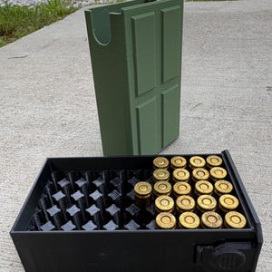 May include: A matte black rectangular ammunition storage tray with a grid of circular slots, partially filled with brass-cased 9mm Luger cartridges. Behind the tray stands an olive green, rectangular, door-shaped storage container.
