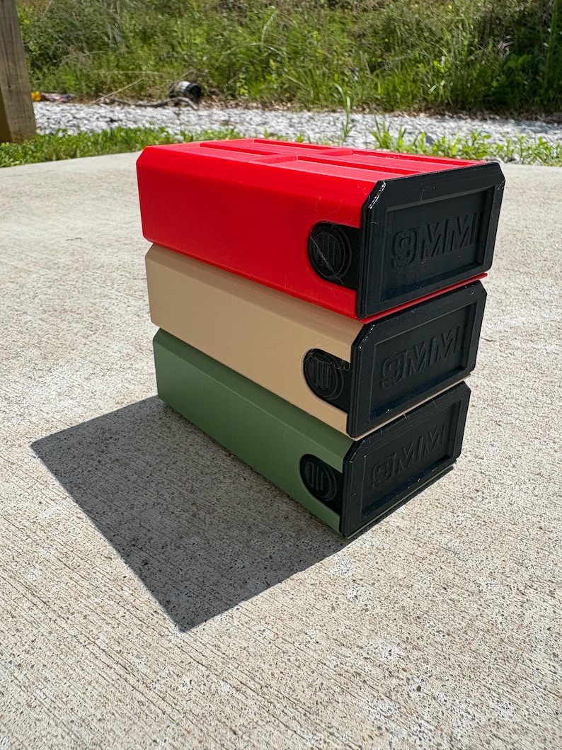 May include: A stack of three rectangular storage containers in red, tan, and olive green. Each container features a black front panel with the embossed text 9MM and a circular side dial mechanism. The units are stacked vertically on a concrete surface.