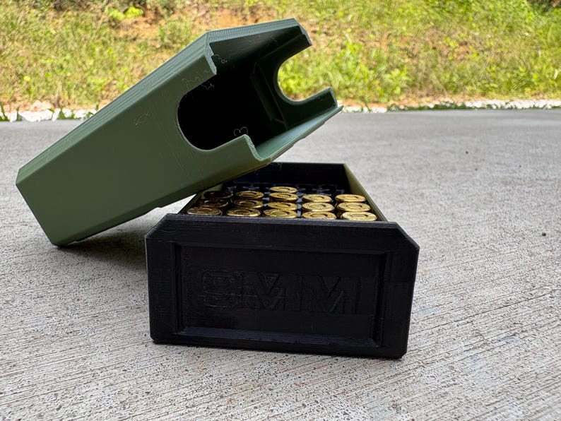May include: An olive green plastic storage case with a removable lid, containing multiple brass-colored cartridges. The black front panel of the base features the embossed text 9MM, indicating the caliber of the ammunition stored inside the container.