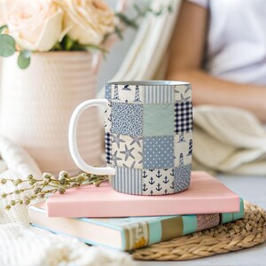 Puede incluir: Taza de cer&aacute;mica blanca con un dise&ntilde;o de patchwork con patrones n&aacute;uticos azules y blancos, que incluyen anclas, faros y estrellas de mar. La taza tiene un asa blanca y est&aacute; sobre dos libros.