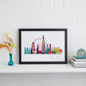 May include: A black framed print of a colorful London skyline with the London Eye, Big Ben, and the Shard. The print is on a white background and has a handwritten signature in the bottom right corner.