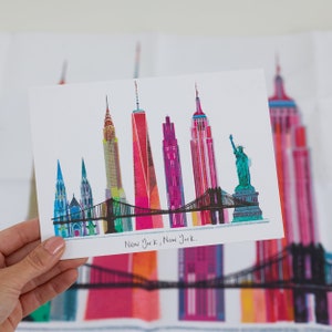 Puede incluir: Una ilustraci&oacute;n colorida del horizonte de la ciudad de Nueva York, con monumentos emblem&aacute;ticos como el Empire State Building, el Chrysler Building y la Estatua de la Libertad. La ilustraci&oacute;n est&aacute; sobre un fondo blanco e incluye el texto "New York, New York."