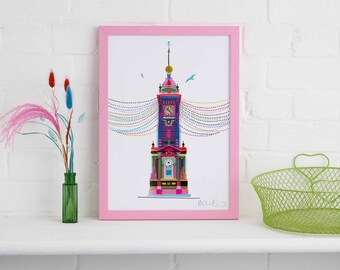 May include: A pink framed print of a colorful illustration of a clock tower with a string of colorful lights above it. The print is on a white shelf with a green wire basket and a vase with pink and blue flowers.