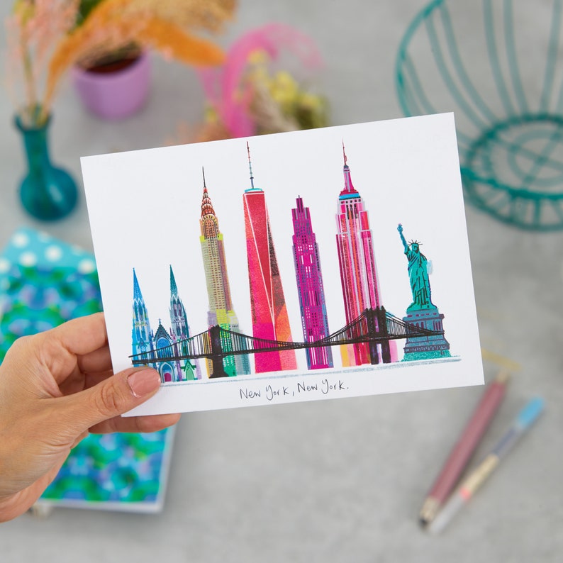 Puede incluir: Una ilustraci&oacute;n colorida del horizonte de la ciudad de Nueva York, con monumentos emblem&aacute;ticos como el Empire State Building, el Chrysler Building y la Estatua de la Libertad. El texto "New York, New York." est&aacute; escrito debajo de la ilustraci&oacute;n.