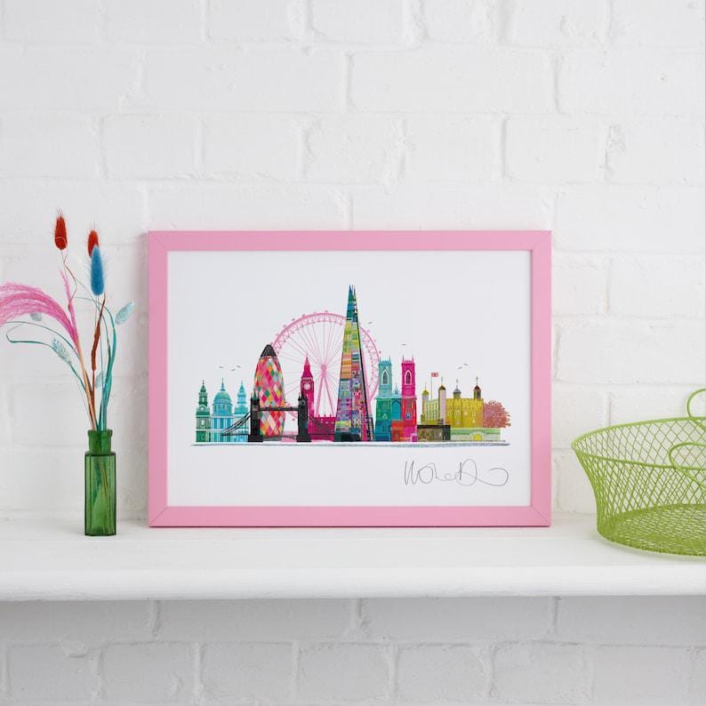 May include: A pink framed print of a colorful London skyline with the London Eye, Big Ben, and the Shard. The print is signed "Woolf" in the bottom right corner.