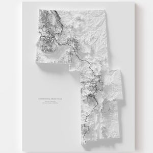 May include: A white, three-dimensional relief map of a geographical area, possibly a state or region. The map features detailed topographical lines in black, with the text "Continental Divide Trail" and other text at the bottom. The map is mounted on a white surface.