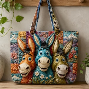 Könnte beinhalten: Eine gesteppte Tragetasche mit dreidimensionalen Eselköpfen in Orange, Blau und Grün. Der Hintergrund besteht aus einem Patchwork aus bunten Blumen- und Landschaftsmustern. Die Tasche hat zwei passende Stoffgriffe und eine rechteckige Form.