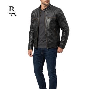 Puede incluir: Chaqueta de cuero negra con cuello alzado y detalles acolchados en los hombros. La chaqueta tiene cierre de cremallera y múltiples bolsillos. El modelo lleva una camiseta gris y vaqueros azul oscuro. La chaqueta es de la marca "Belted Attire".