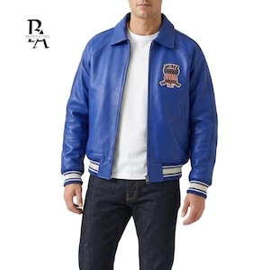 Könnte beinhalten: Eine leuchtend blaue Lederjacke mit klassischem Kragen und Reißverschluss. Die Jacke hat einen Aufnäher auf der Brust und gestreifte Details an den Manschetten und am Saum. Dazu wird eine dunkle Jeans getragen.