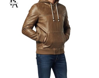 May include: Brown leather hoodie with a kangaroo pocket and drawstring hood. The jacket has a ribbed hem and cuffs. The logo "BELTED ATTIRE" is in the upper left corner. The model is wearing blue jeans.