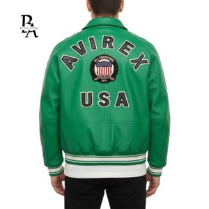 May include: Green leather jacket with white trim and the text "AVIREX USA" on the back. The jacket features a circular patch with the American flag and the words "All Americans" and "1975". The jacket has a classic bomber style.