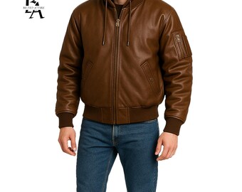 May include: A brown leather bomber jacket with a hood and a zipper closure. The jacket has a ribbed hem and cuffs, and a pocket on the left sleeve. The jacket is worn with blue jeans. The logo "BILTED ATTIRE" is visible on the upper left.