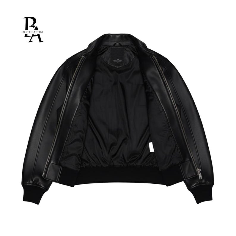 May include: Black leather bomber jacket with a zip closure, ribbed cuffs, and a ribbed hem. The jacket is open, revealing a black interior lining. The brand logo "BELTED ATTIRE" is visible in the upper left corner.