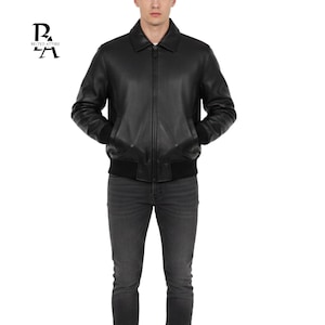 Könnte beinhalten: Schwarze Leder-Bomberjacke mit Kragen, Reißverschluss vorne und gerippten Bündchen und Saum. Die Jacke hat zwei Vordertaschen und wird mit dunkelgrauen Jeans getragen. Das Markenlogo ist sichtbar.