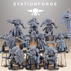 Può includere: Una collezione di figurine in miniatura grigie di soldati corazzati, alcuni con armi e scudi. Le figurine sono su supporti trasparenti. Il testo "STATIONFORGE" e un logo a forma di teschio sono in alto.