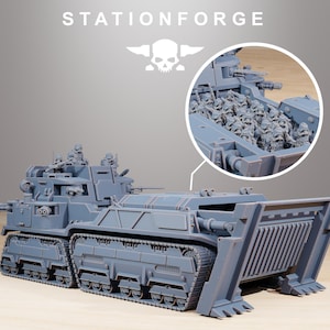 May include: A grey model of a military vehicle, featuring a large front blade and multiple turrets. The vehicle has tank treads and a detailed interior, visible in a circular inset. The text "STATIONFORGE" and a skull logo are at the top.