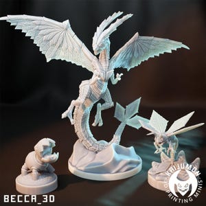 Puede incluir: Tres miniaturas de fantasía blancas impresas en 3D. Un gran dragón con alas extendidas, una pequeña criatura parecida a un insecto y una pequeña figura parecida a un robot. El dragón es la figura central. El texto "BECCA_3D" está en la parte inferior izquierda.