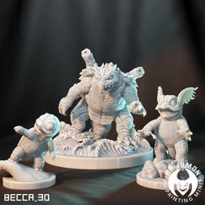 May include: Three white 3D-printed figurines of turtle-like creatures. The largest figure has multiple cannons on its back. The smallest figure is posed on a hand-shaped base. The figures are on white bases. The text "BECCA_3D" is visible.