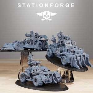 Puede incluir: Tres vehículos de guerra en miniatura grises con armas y figuras montadas. Los vehículos se exhiben sobre soportes negros. La parte superior de la imagen tiene el texto "STATIONFORGE" y un logotipo de calavera.