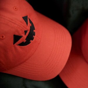 Puede incluir: Dos gorras de béisbol naranjas con un diseño de cara de calabaza negra bordada en la parte delantera. Las gorras están hechas de una tela suave y tienen una visera curva. Un accesorio festivo para Halloween.