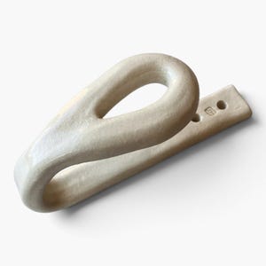 May include: A cream-colored ceramic wall hook with a smooth, glossy finish. The hook features a looped, teardrop-shaped design that extends from a flat, rectangular mounting base. The base includes two circular holes for installation and a small stamp.
