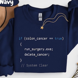 May include: Navy blue sweatshirt with the text "if (colon_cancer == true) { run_surgery.exe; delete_cancer; } // System Clear" in a computer code style. A gold star pendant necklace is draped across the front.