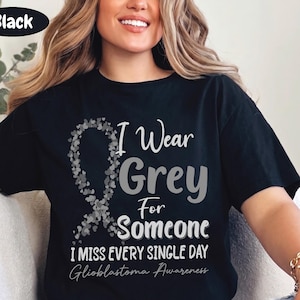 May include: A black short-sleeve t-shirt featuring a grey awareness ribbon made of small hearts. The text reads: I Wear Grey For Someone I MISS EVERY SINGLE DAY Glioblastoma Awareness. The design is printed in shades of grey and white on the front.