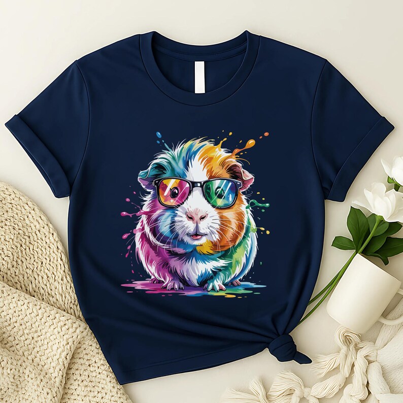 May include: Navy blue t-shirt featuring a colorful guinea pig wearing sunglasses. The guinea pig has a rainbow-colored coat with splashes of paint around it. The t-shirt is knotted at the bottom.