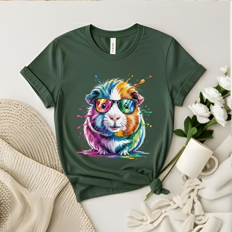 May include: A dark green t-shirt featuring a colorful guinea pig wearing sunglasses. The guinea pig has a rainbow-colored design with paint splatter effects. The shirt has a crew neck and short sleeves.