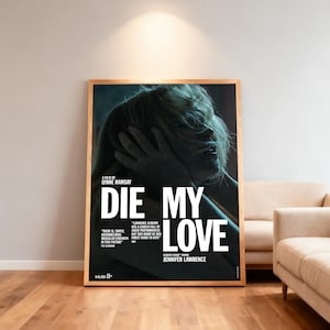 May include: A framed poster for the film "Die My Love" starring Jennifer Lawrence. The poster, in a wooden frame, displays the title in large white letters. The image shows a woman with her hands on her face. The poster is leaning against a wall.