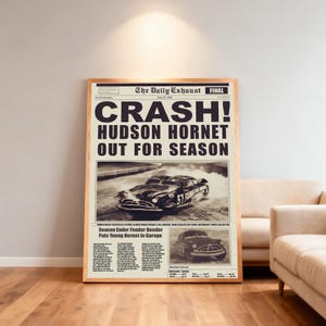 May include: A framed vintage newspaper print with the headline "CRASH! HUDSON HORNET OUT FOR SEASON." The sepia-toned image features a classic car and text. The wooden frame adds a classic touch to the artwork.