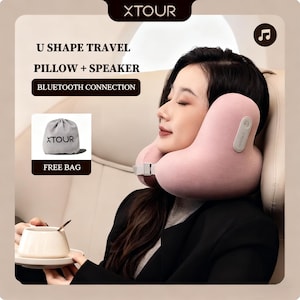 May include: A pink U-shaped travel pillow with a speaker, featuring Bluetooth connection. The image also shows a gray drawstring bag with the text "XTOUR" and the words "FREE BAG". The pillow is around a person's neck.