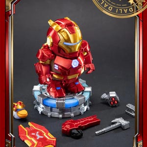 May include: A red and gold Iron Man figurine on a blue light-up base. The figure has a detailed design and is surrounded by miniature accessories, including a hammer and a shield. The image is framed with a red border.