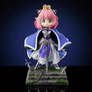 Puede incluir: Figura de un personaje con cabello rosado, ojos verdes y una corona dorada. La figura lleva una capa azul con ribete blanco, armadura plateada y sostiene una espada. Varias espadas están colocadas en la base.