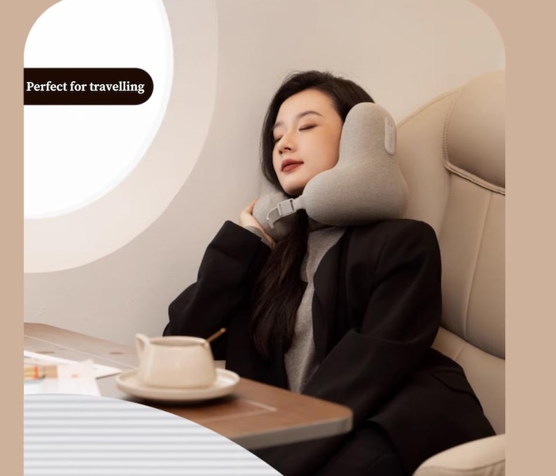 May include: A gray travel neck pillow is around a person's neck. The person is sitting in a plane seat, with a cup of coffee on a tray table. The text "Perfect for travelling" is in the upper left corner.