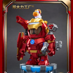 May include: A red and gold action figure of a duck in an Iron Man-style suit, standing on a blue and grey platform. The figure has a gold helmet and chest plate, with red armour. The figure is holding a shield and a weapon. The background is a dark grey.