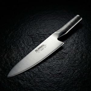 May include: A stainless steel chef's knife with a textured handle and a sharp blade. The knife has the word "GLOBAL" printed on the blade. The knife is on a black surface.