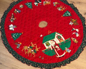May include: A round, quilted Christmas tree skirt with a red background and a green ruffled edge. The skirt features embroidered images of Santa Claus, reindeer, Christmas trees, and other festive characters. The center has a hole for the tree trunk.