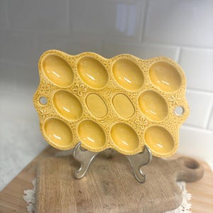 May include: A set of three ceramic mugs with a speckled, matte finish. The mugs are in shades of cream, light gray, and dark gray. Each mug has a simple, minimalist design and a rounded handle.