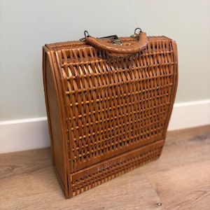 May include: A rectangular brown wicker basket with a curved top and a woven handle. The basket features a hinged lid with a metal latch mechanism at the top and a flat base, constructed from natural woven reeds in a vertical pattern.